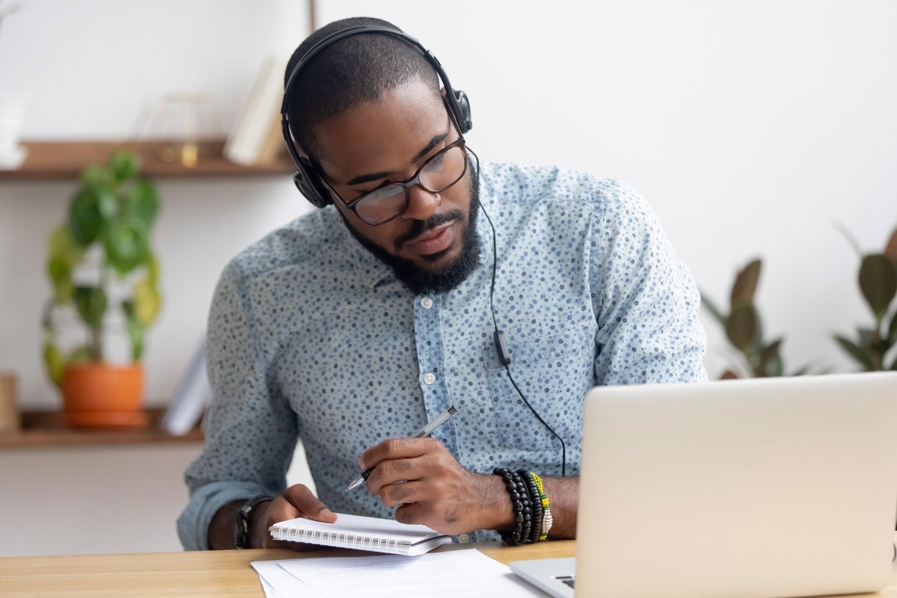 Male Student Listening To Lecture On Latop And Taking Notes